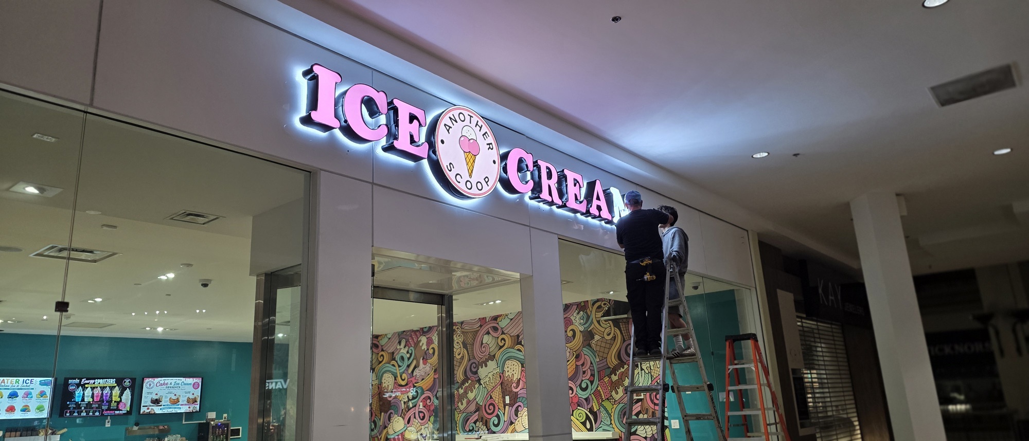 Two Neon City and Signs installers on ladders setting the ICE CREAM letters